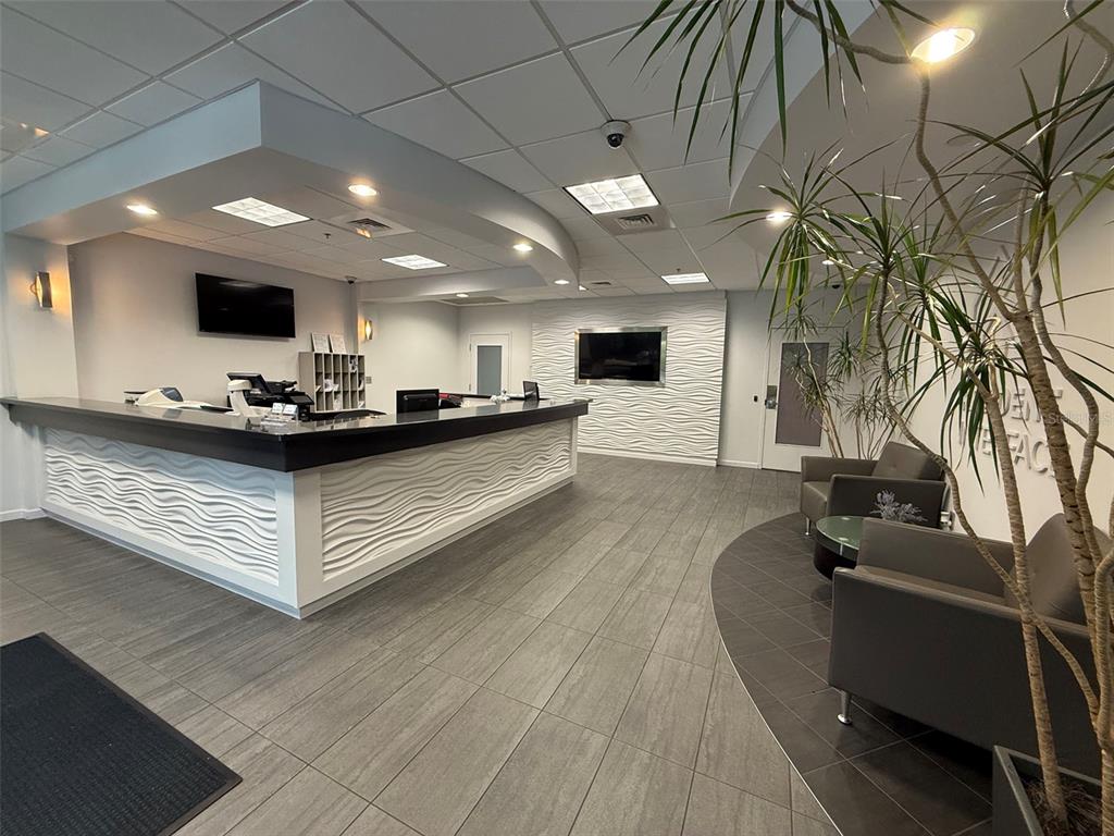 A modern office reception area features a white wavy-textured desk, gray tile flooring, and seating — 4620 WOODLAND CORPORATE BOULEVARD, TAMPA, FL