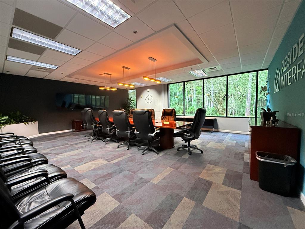 A conference room features a long wooden table, leather chairs, and large windows overlooking trees — 4620 WOODLAND CORPORATE BOULEVARD, TAMPA, FL