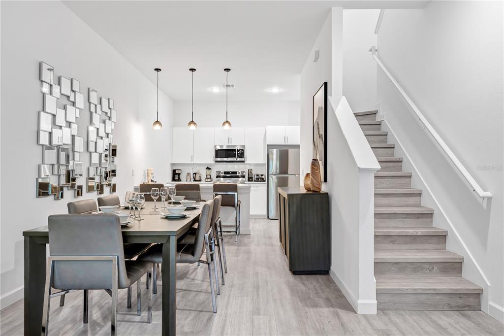 A modern dining area and kitchen feature light wood flooring, white cabinetry, and a staircase — 396 FAMAGUSTA DRIVE, DAVENPORT, FL