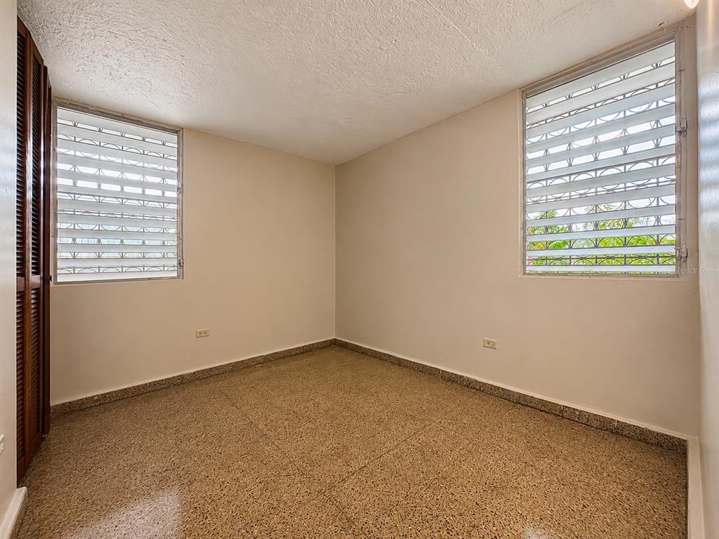 An empty room with beige walls, speckled tile flooring, and two louvered windows — #1 ST. URB. VILLA ARRIETA 1ST FLOOR UNIT C-51, BAYAMON, PR