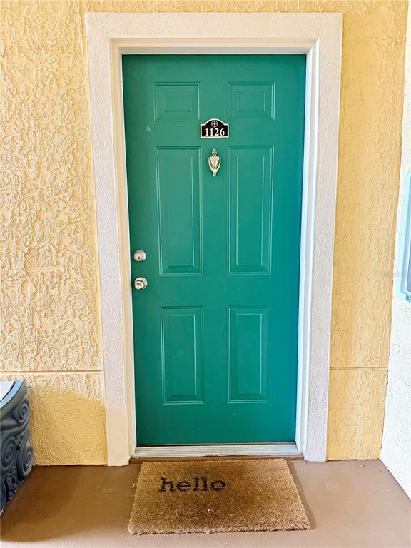 A teal front door with a door knocker and number plate sits in a yellow wall — 2747 VIA CAPRI UNIT 1126, CLEARWATER, FL