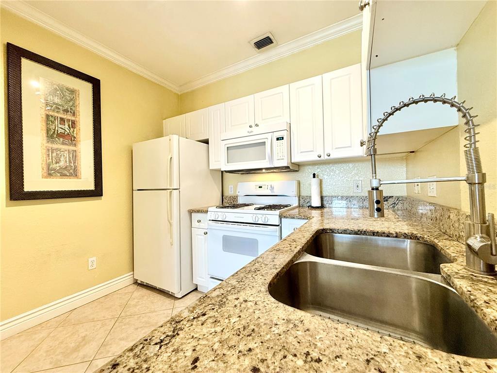 A kitchen features white cabinets, white appliances, granite countertops, and a double stainless steel sink — 2747 VIA CAPRI UNIT 1126, CLEARWATER, FL