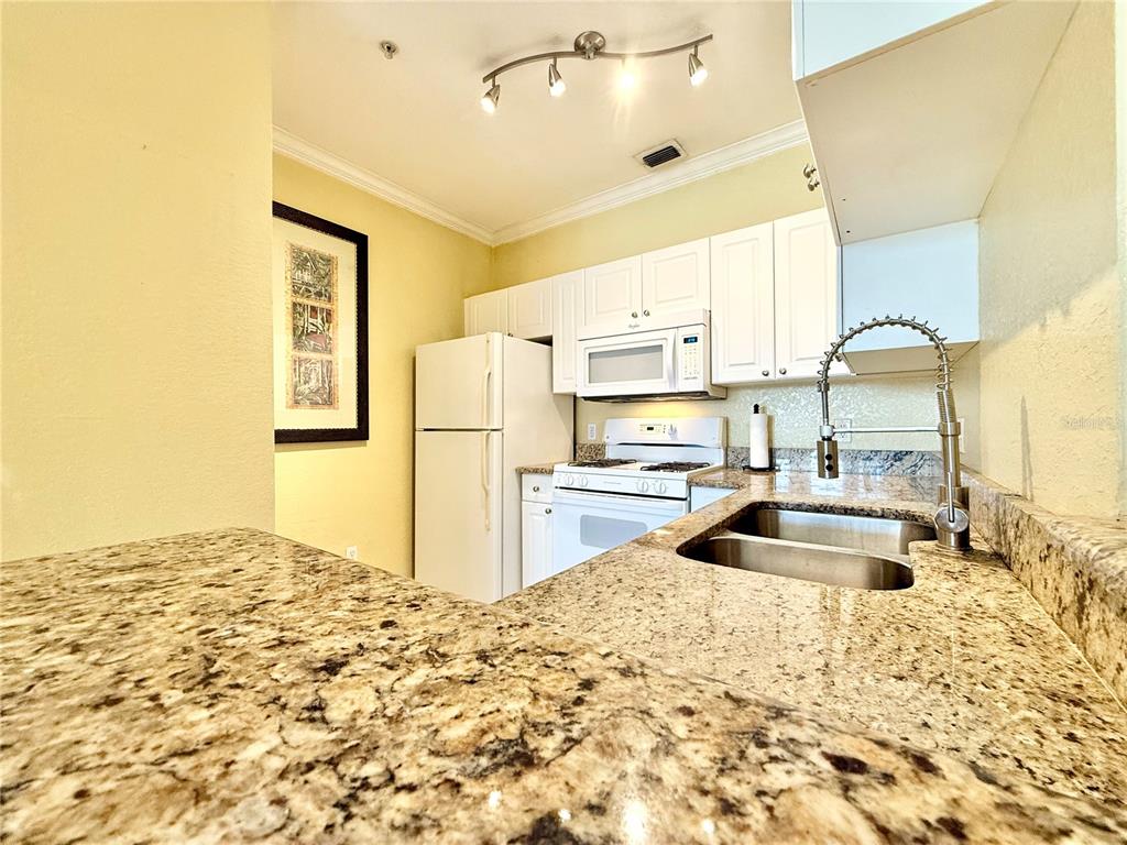 A kitchen features granite countertops, white cabinetry, a double sink, and white appliances — 2747 VIA CAPRI UNIT 1126, CLEARWATER, FL