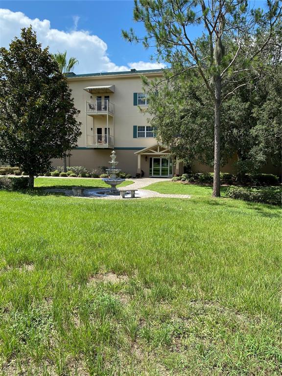 A multi-story building with balconies and a central fountain sits behind a grassy lawn — 8176 SOUTHERN PINES DRIVE UNIT 8176, BROOKSVILLE, FL