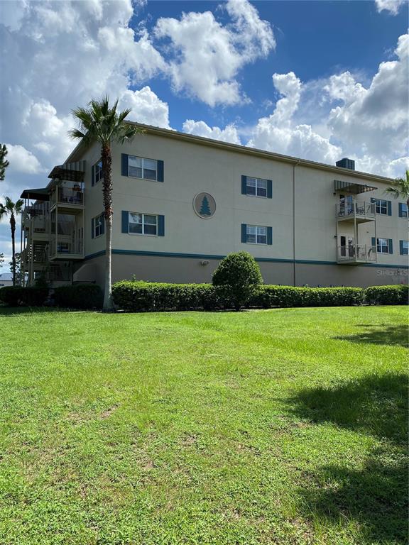 A three-story apartment building features beige stucco walls, blue shutters, and exterior balconies — 8176 SOUTHERN PINES DRIVE UNIT 8176, BROOKSVILLE, FL