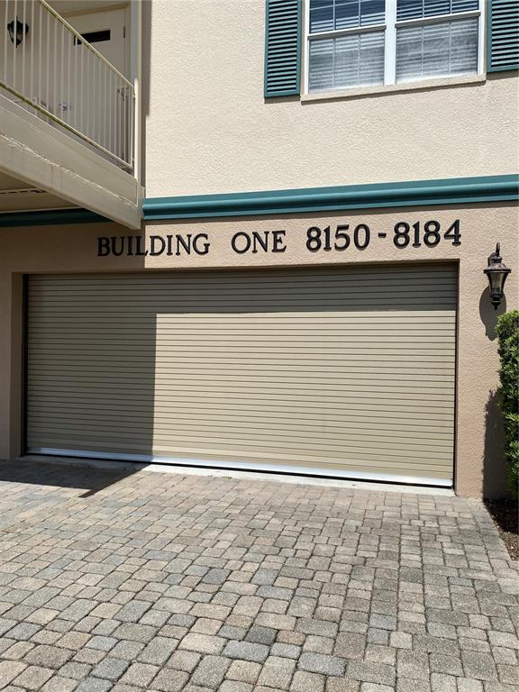 A beige building exterior features a large roll-up garage door and a paved driveway — 8176 SOUTHERN PINES DRIVE UNIT 8176, BROOKSVILLE, FL