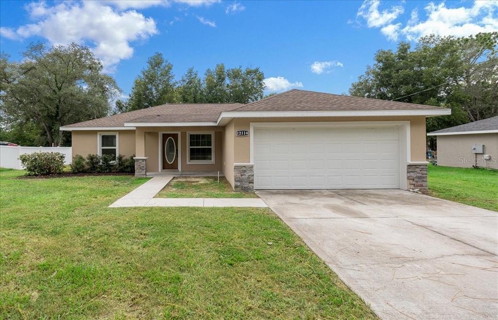 A single-story house with a tan exterior, a two-car garage, and a concrete walkway — 12114 SE 87TH TERRACE, BELLEVIEW, FL