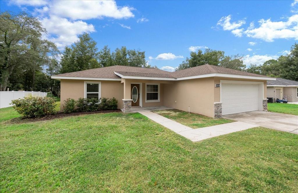 A single-story house with a tan stucco exterior, a brown roof, and a two-car garage — 12114 SE 87TH TERRACE, BELLEVIEW, FL