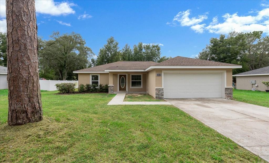 A single-story house with a tan exterior, a two-car garage, and a concrete driveway — 12114 SE 87TH TERRACE, BELLEVIEW, FL