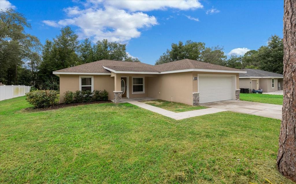 A single-story house with a tan stucco exterior, a two-car garage, and a front lawn — 12114 SE 87TH TERRACE, BELLEVIEW, FL