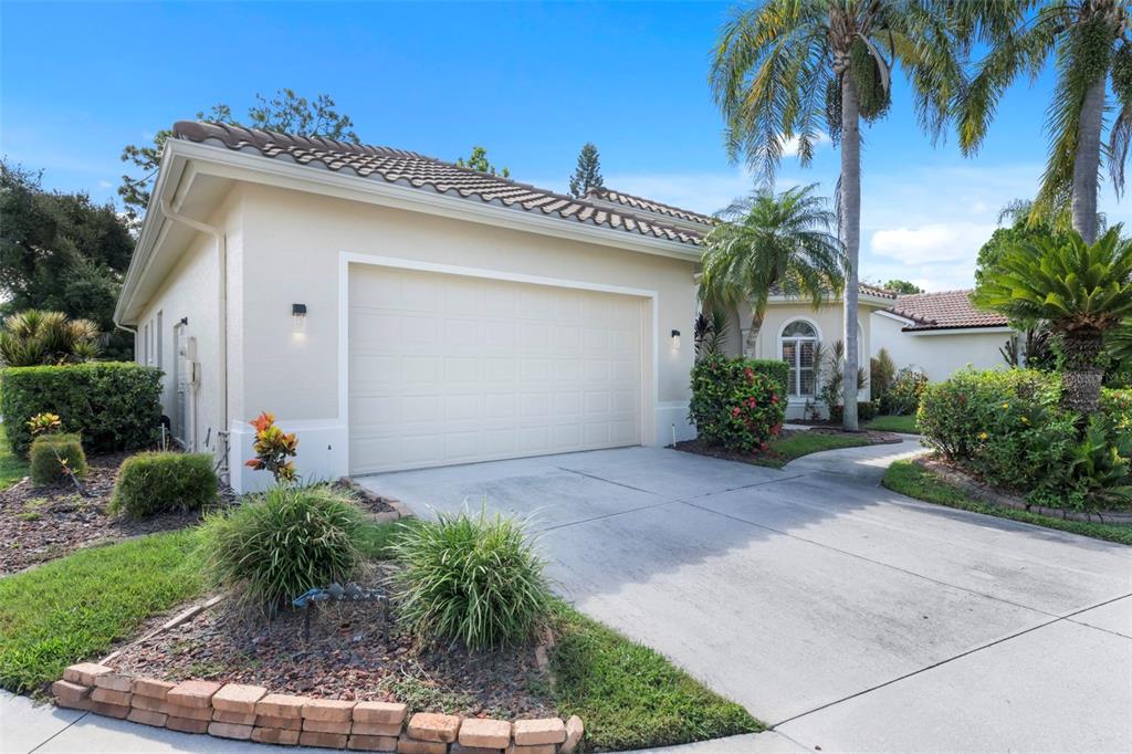 A beige house with a two-car garage, a concrete driveway, and tropical landscaping — 8809 HAVENRIDGE DRIVE, SARASOTA, FL