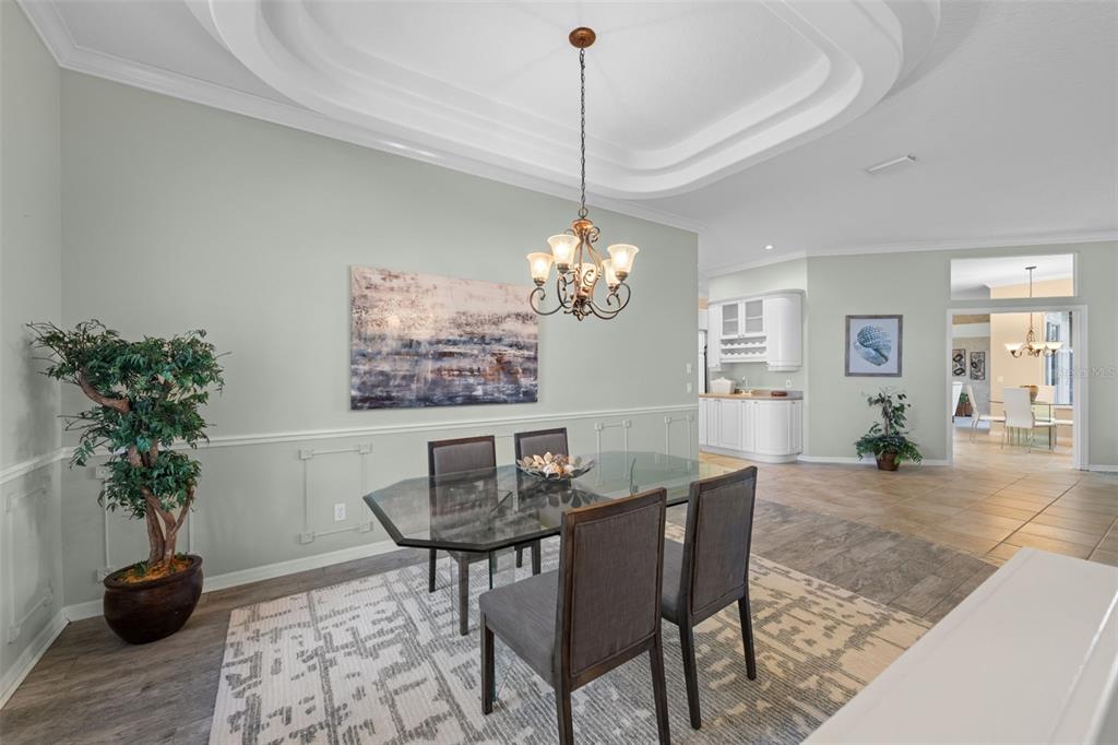 A dining room features a glass table, gray chairs, a chandelier, and a tray ceiling — 8809 HAVENRIDGE DRIVE, SARASOTA, FL