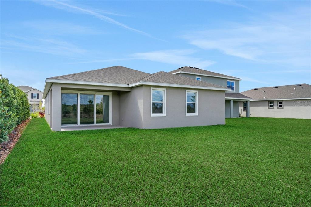 The exterior of a single-story house features a gray stucco finish, sliding glass doors, and lawn — 13470 TURNLEAF BOULEVARD, PUNTA GORDA, FL