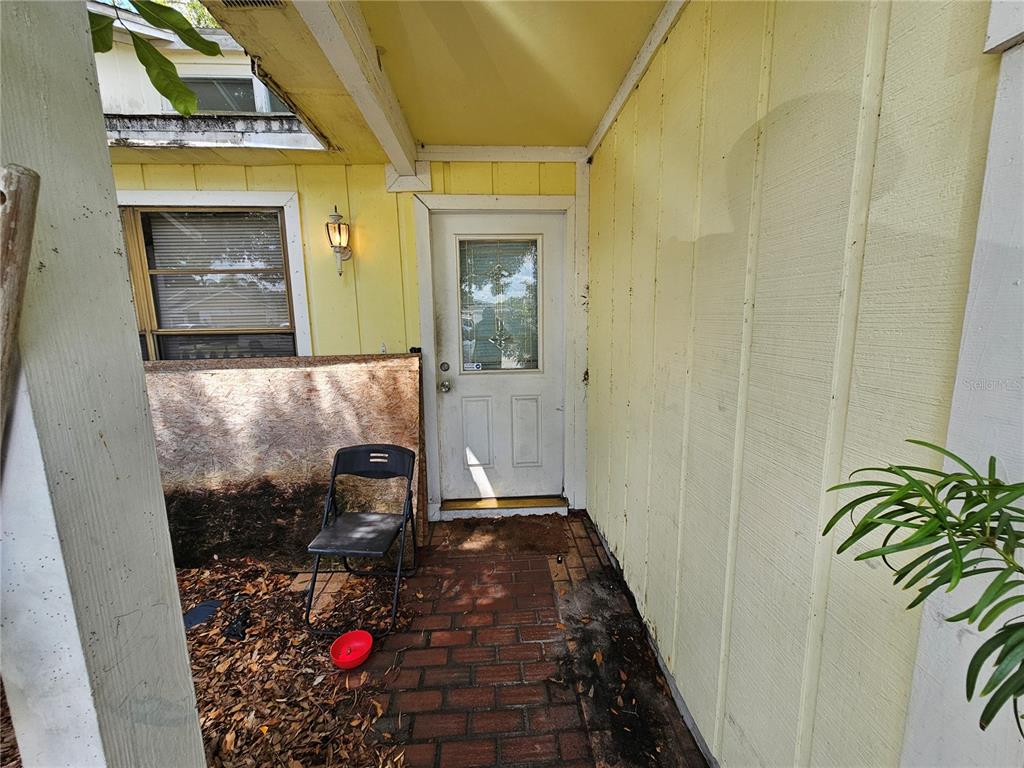 An exterior view of a yellow-sided house entrance with a brick porch and folding chair — 4153 LANCASTER DRIVE, SARASOTA, FL
