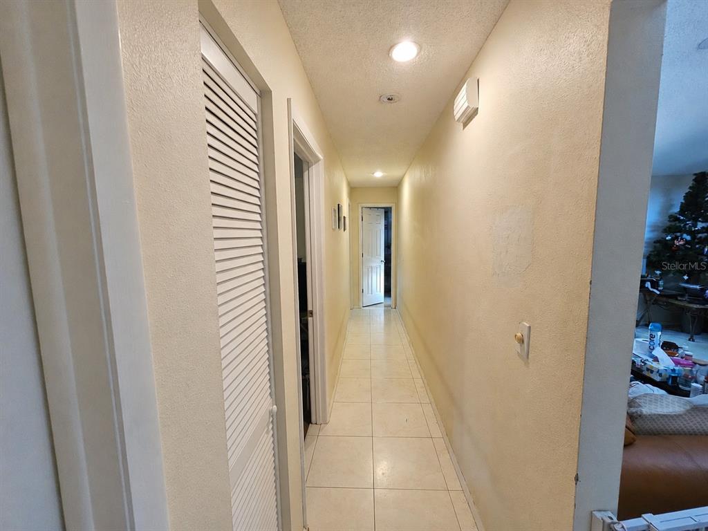 A hallway with light-colored tile flooring, white walls, and a louvered closet door — 4153 LANCASTER DRIVE, SARASOTA, FL