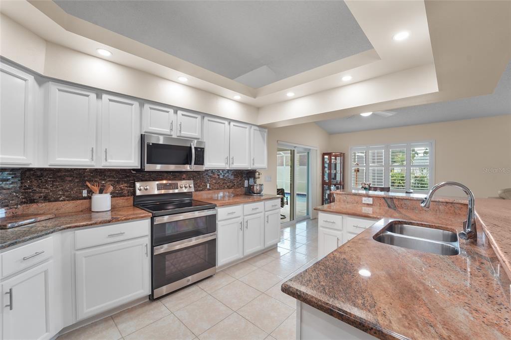 A kitchen features white cabinets, granite countertops, a tile backsplash, and stainless steel appliances — 9110 FLAGSTICK LANE, HUDSON, FL