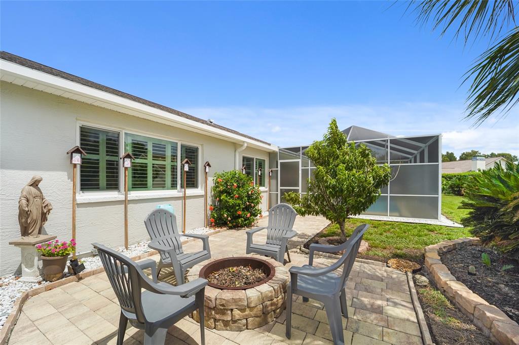 A stone fire pit sits on a paved patio with four chairs beside a house — 9110 FLAGSTICK LANE, HUDSON, FL