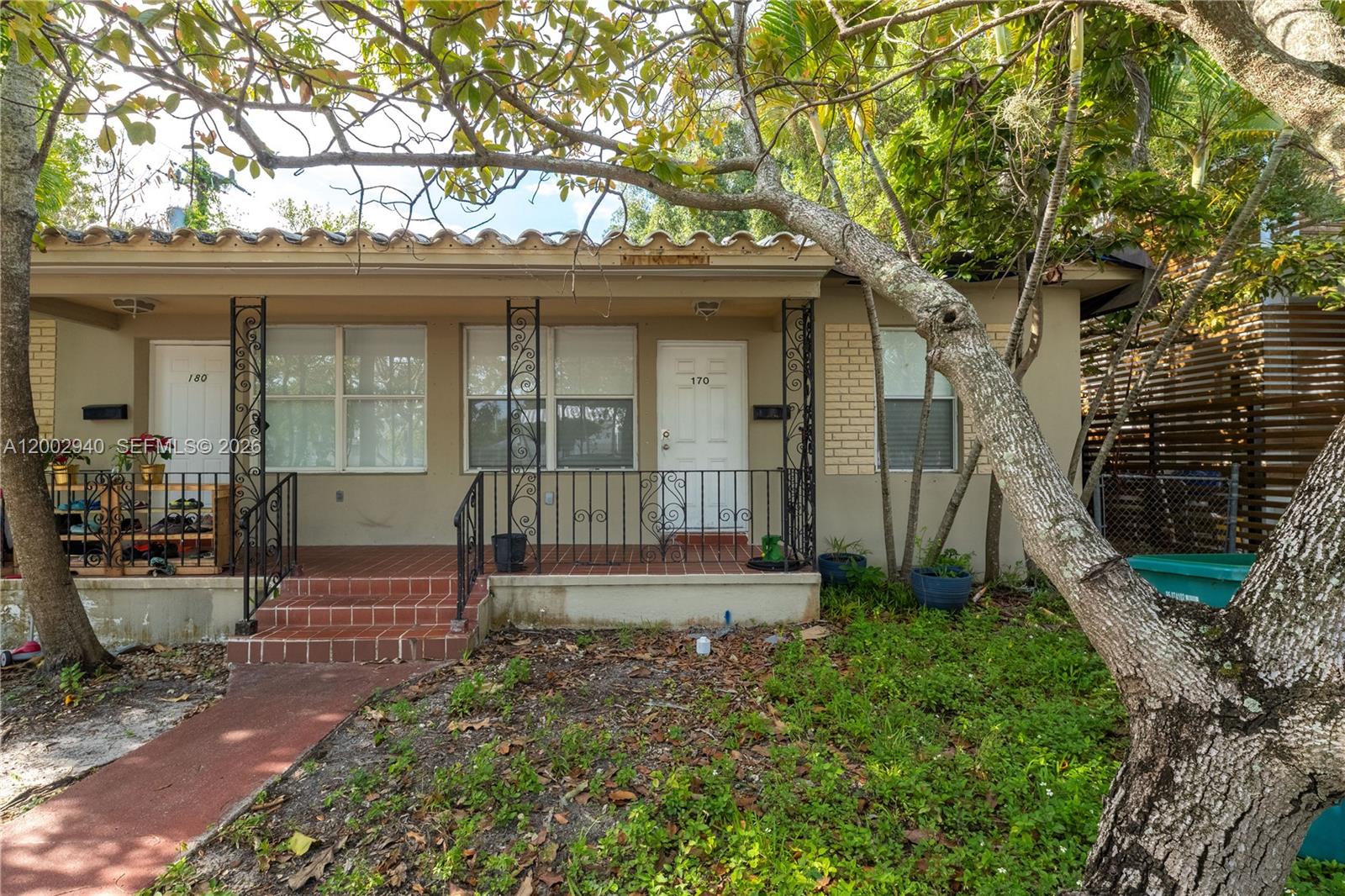 The exterior of a single-story duplex features a tiled porch, wrought iron railings, and trees — 170 NE 48th St, Miami FL 33137, MIAMI, FL