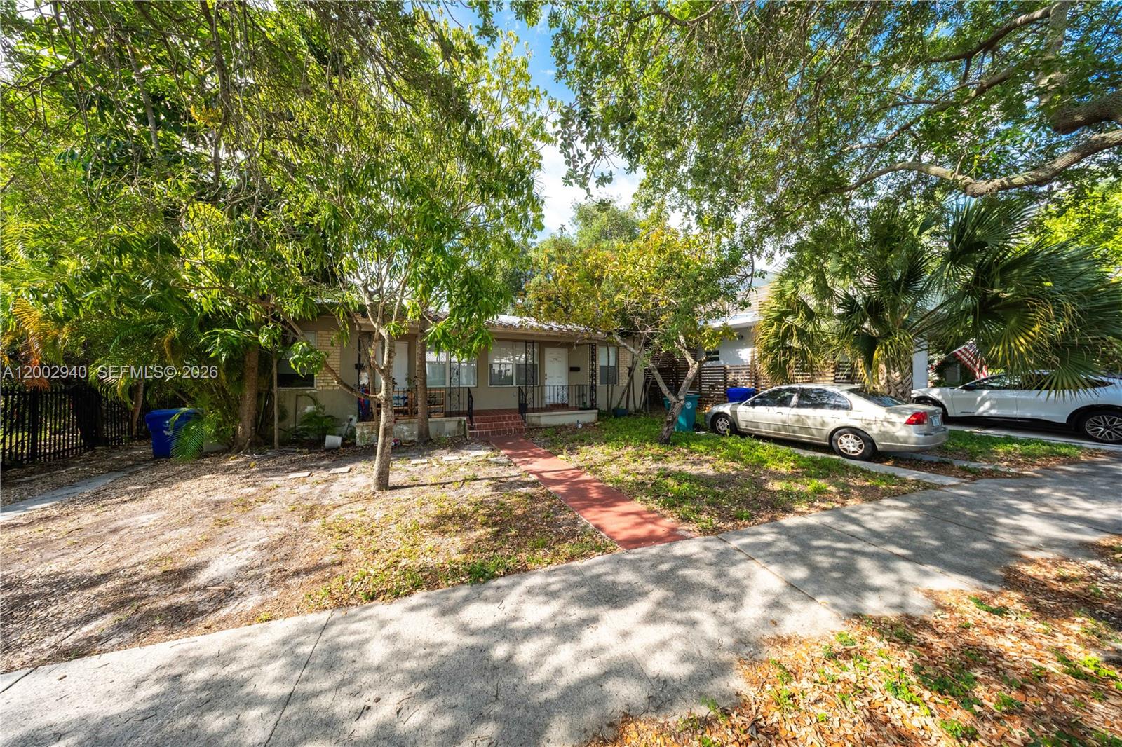 A single-story house with a red walkway and parked cars sits behind mature trees — 170 NE 48th St, Miami FL 33137, MIAMI, FL