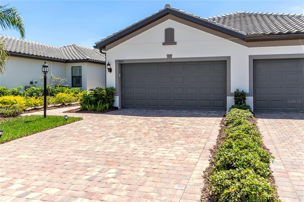 A paved driveway leads to the garage of a single-story house with a tiled roof — 7660 SUMMERLAND COVE, BRADENTON, FL
