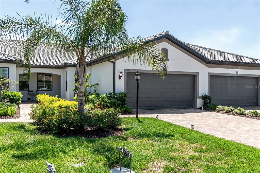 A single-story house exterior features a gray two-car garage, a palm tree, and landscaping — 7660 SUMMERLAND COVE, BRADENTON, FL