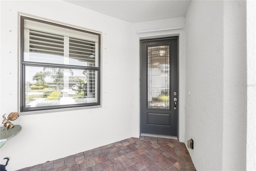 A covered entryway features a dark gray front door with glass inlay and a window — 7660 SUMMERLAND COVE, BRADENTON, FL