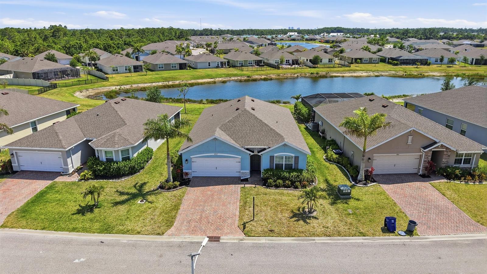 An aerial view shows three suburban houses with paved driveways facing a small pond — 8909 Cascade Price Circle, FL 33917, FL