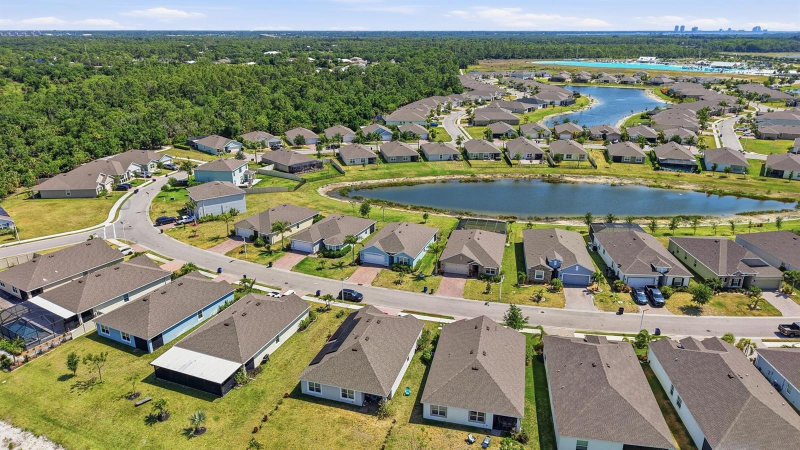 An aerial view shows a suburban neighborhood with single-family homes surrounding a central pond — 8909 Cascade Price Circle, FL 33917, FL
