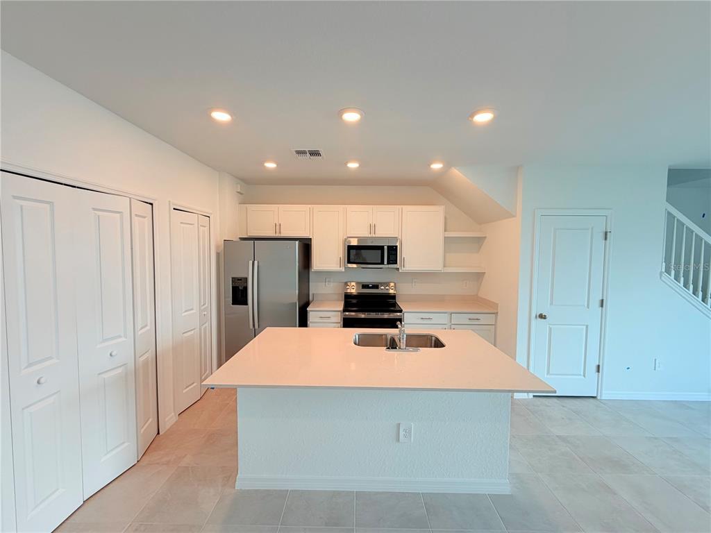 A kitchen features white cabinets, stainless steel appliances, a central island, and light tile flooring — 14538 LILAC SKY TERRACE, BRADENTON, FL