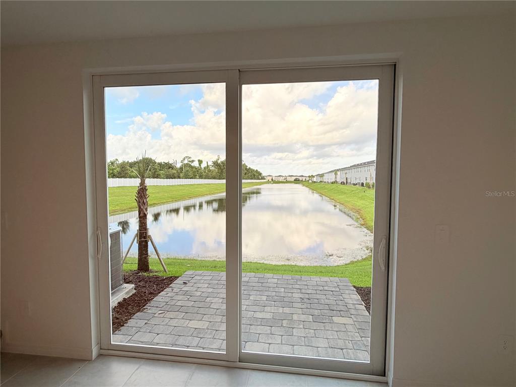 A sliding glass door opens to a paved patio overlooking a pond and residential neighborhood — 14538 LILAC SKY TERRACE, BRADENTON, FL