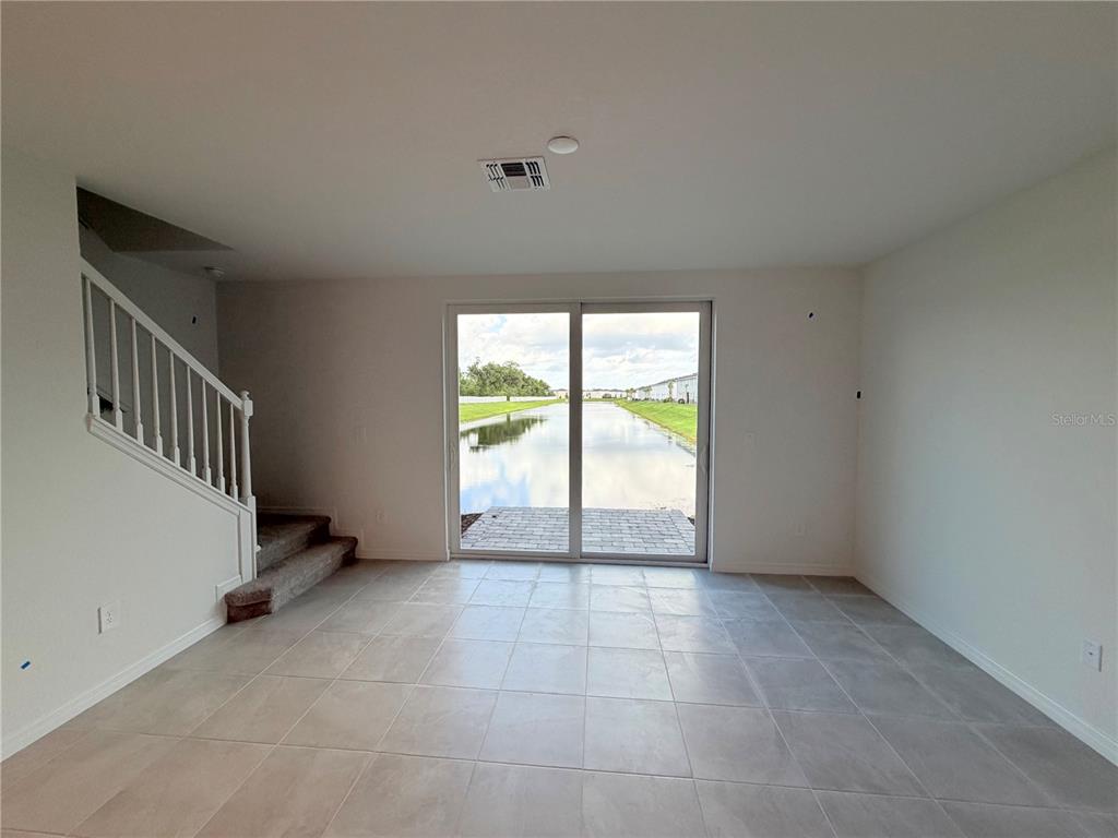A room with tile flooring and a staircase leads to a sliding door overlooking water — 14538 LILAC SKY TERRACE, BRADENTON, FL