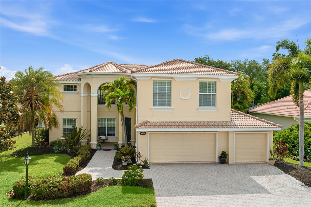 A two-story beige house with a tile roof, three-car garage, and a paved walkway — 6971 SCRUB JAY DRIVE, SARASOTA, FL