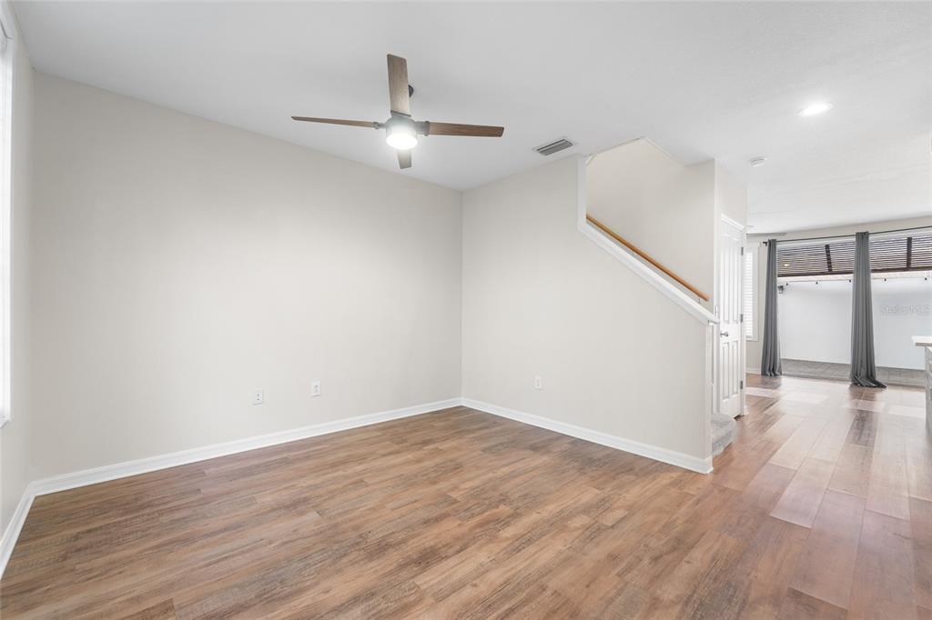 An empty room with wood-look flooring, a ceiling fan, and stairs leading to an upper level — 10007 BRADWELL PLACE, TAMPA, FL
