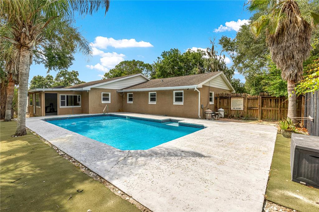 A backyard swimming pool sits on a concrete patio next to a tan house exterior — 11547 SE 123 ST, BELLEVIEW, FL