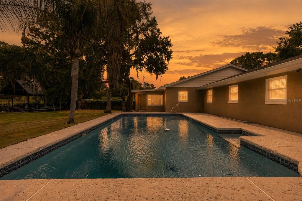 A rectangular swimming pool sits in the backyard of a house at sunset — 11547 SE 123 ST, BELLEVIEW, FL