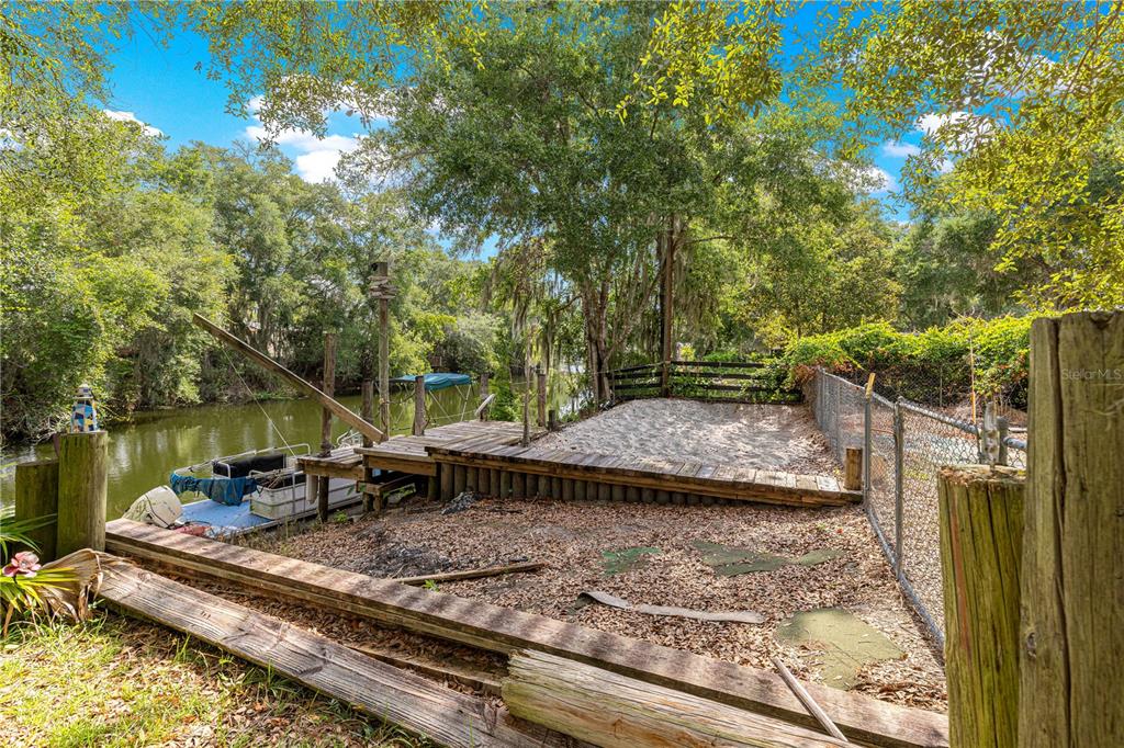 A wooden dock and sandy area sit beside a canal with a moored pontoon boat — 11547 SE 123 ST, BELLEVIEW, FL