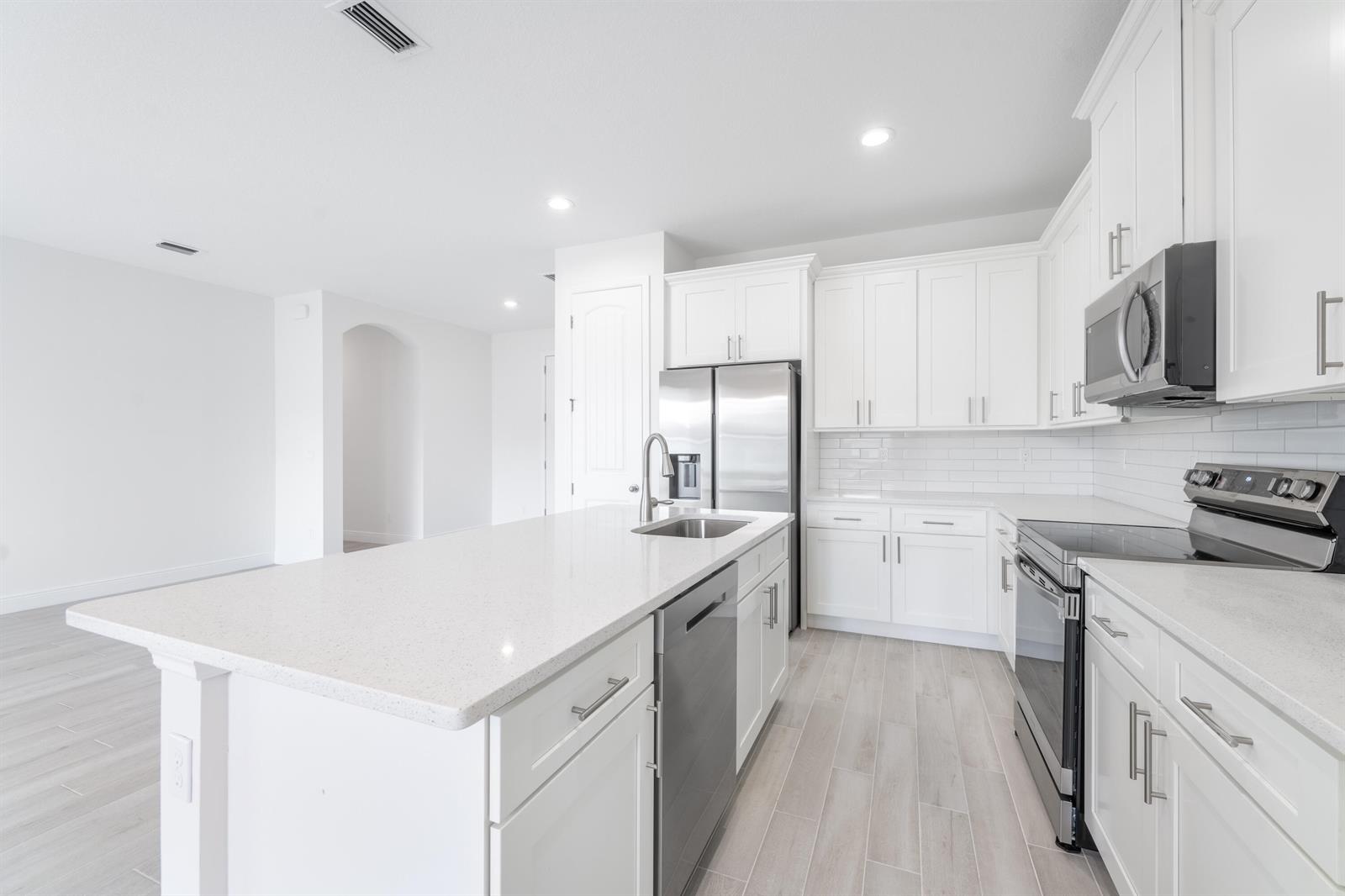 A modern kitchen features white cabinetry, stainless steel appliances, a quartz island, and light flooring — 7103 Citrus Park Boulevard, Fort Pierce FL 34951, FORT PIERCE, FL