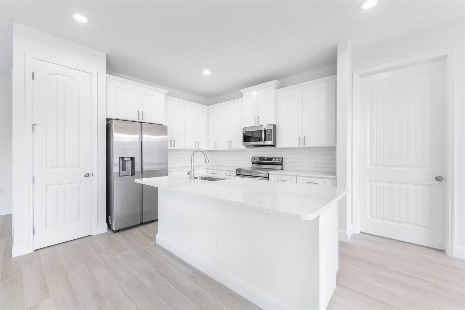 A modern kitchen features white cabinetry, stainless steel appliances, and a central quartz-topped island — 7103 Citrus Park Boulevard, Fort Pierce FL 34951, FORT PIERCE, FL