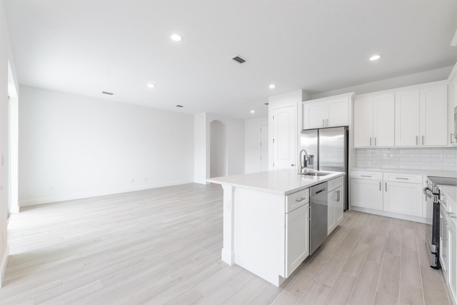 A bright kitchen with white cabinets and a center island opens to a living area — 7103 Citrus Park Boulevard, Fort Pierce FL 34951, FORT PIERCE, FL