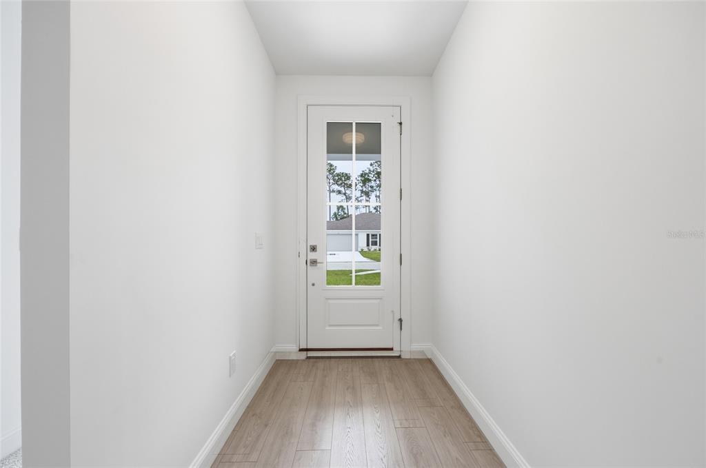 A narrow entryway features white walls, light wood-look flooring, and a glass-paneled front door — 5 REINE PLACE, PALM COAST, FL