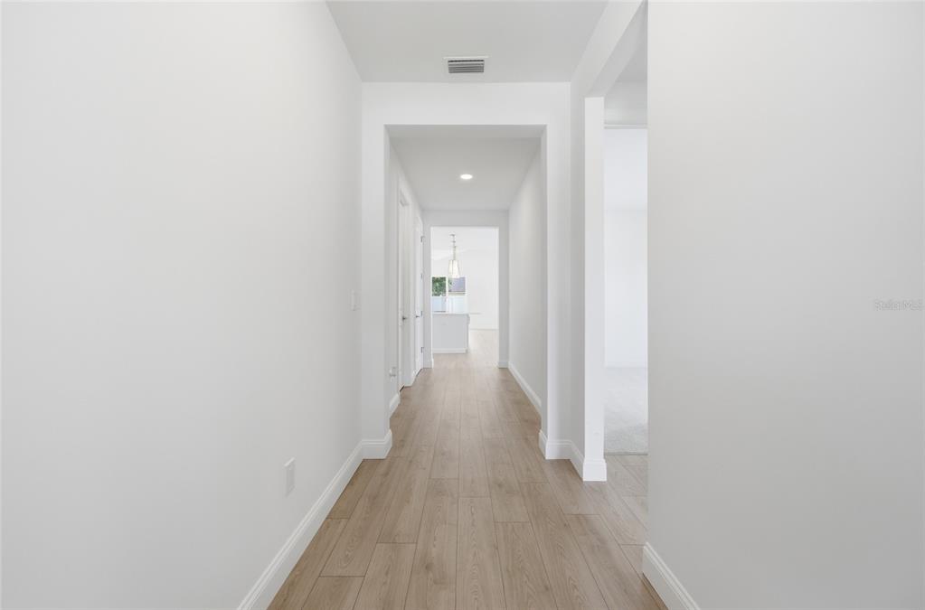 A bright hallway with light wood-look flooring leads toward an open kitchen area — 5 REINE PLACE, PALM COAST, FL