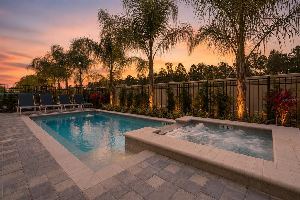 A swimming pool and hot tub sit on a paved patio at sunset with palm trees — 481 LASSO DRIVE, KISSIMMEE, FL