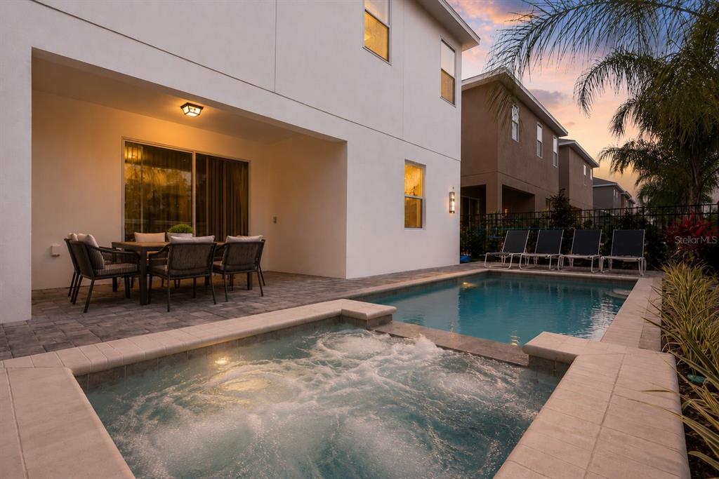 A patio with a dining set overlooks a swimming pool and an attached hot tub — 481 LASSO DRIVE, KISSIMMEE, FL