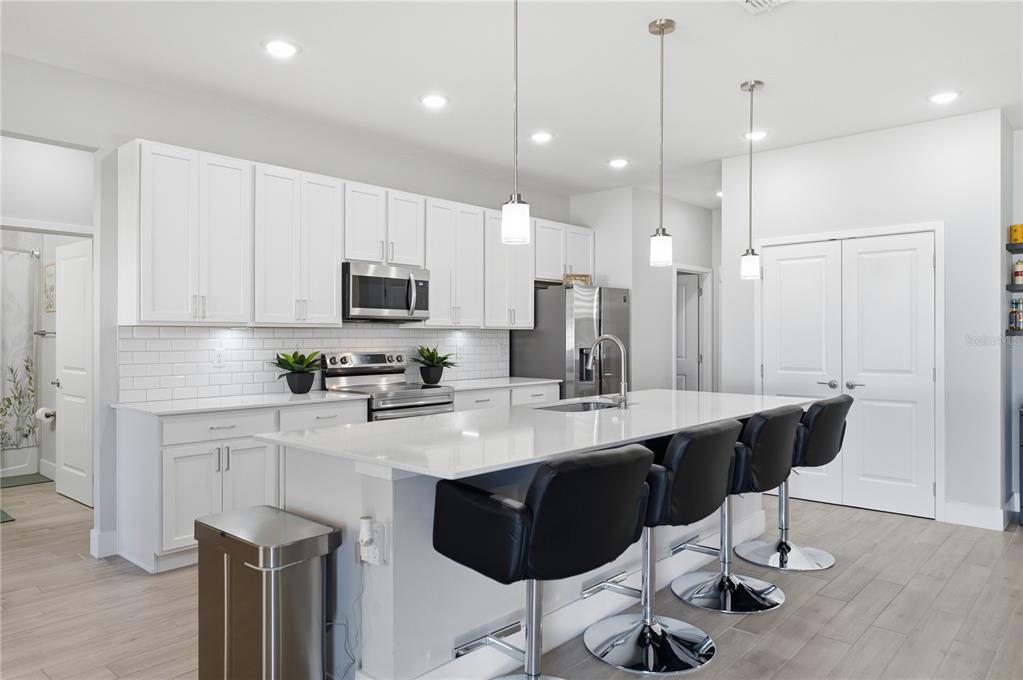 A modern kitchen features white cabinetry, a large quartz island with bar stools, and stainless appliances — 2228 BANCROFT BOULEVARD, ORLANDO, FL