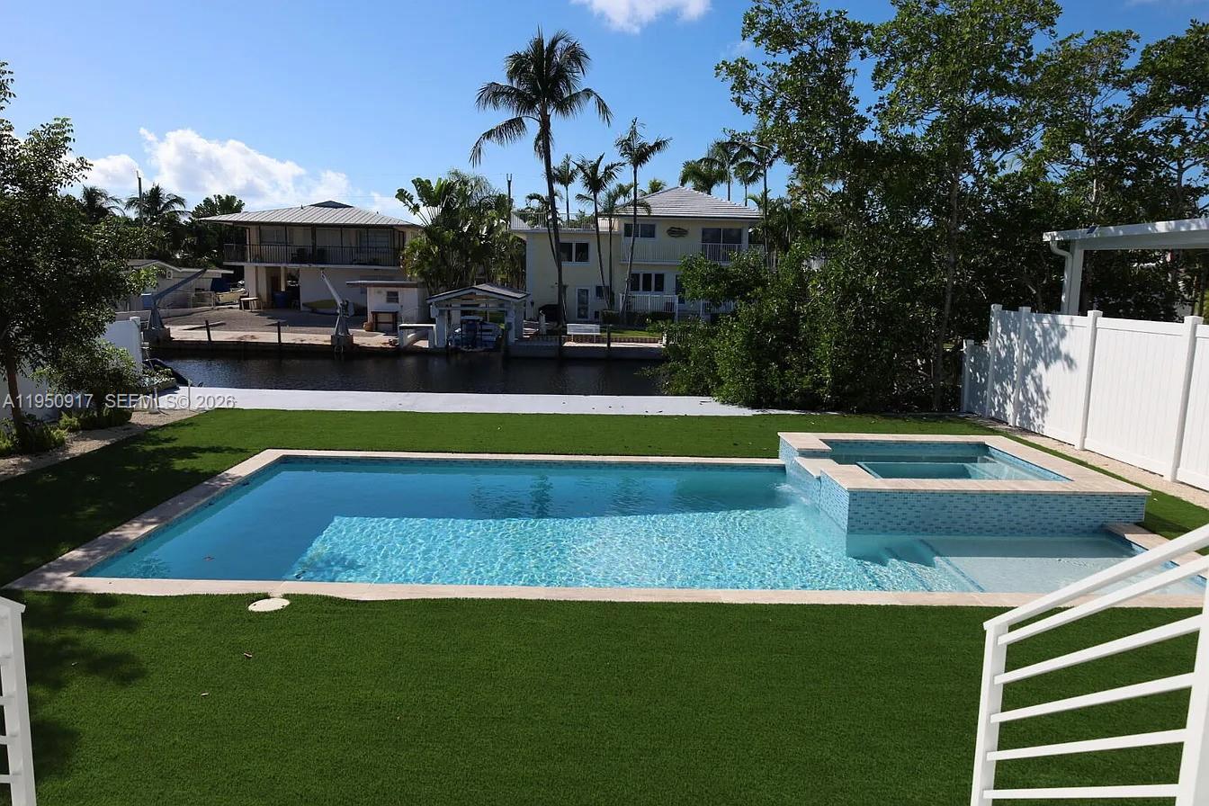 A rectangular swimming pool and attached spa sit in a backyard with artificial turf — 115 Azalea St, Plantation Key FL 33070, PLANTATION KEY, FL