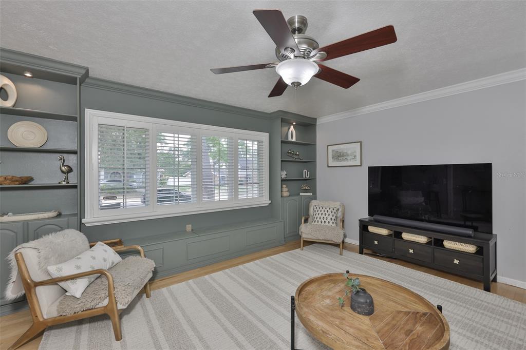 A living room features a window seat between built-in shelves, a ceiling fan, and a television — 1311 ESTATEWOOD DRIVE, BRANDON, FL