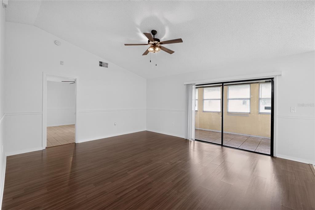 A living room with white walls, dark wood-look flooring, a ceiling fan, and sliding glass doors — 511 BASIL COURT, POINCIANA, FL