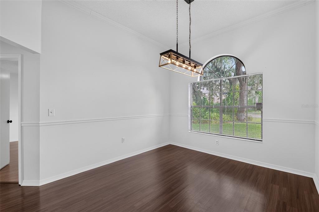 An empty dining room features dark wood flooring, white walls with wainscoting, and a pendant light — 511 BASIL COURT, POINCIANA, FL