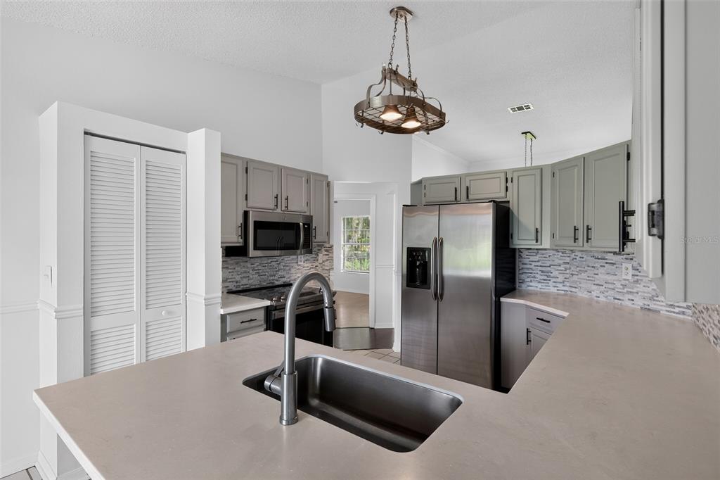 A kitchen features gray cabinets, stainless steel appliances, a center island with a sink, and pendant lighting — 511 BASIL COURT, POINCIANA, FL