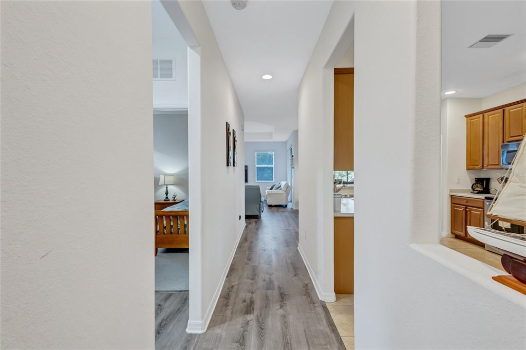 A hallway with wood-look flooring leads from a bedroom toward a kitchen and living area — 9019 HERITAGE SOUND DRIVE, BRADENTON, FL